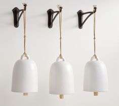 three white lamps hanging from hooks on a wall next to two black and gold lights