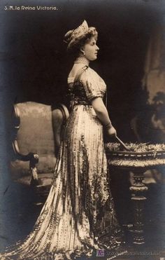 an old photo of a woman in a dress and hat with a cake on a table