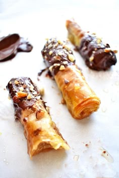 three chocolate covered pastry sticks sitting on top of a white countertop next to melted chocolate