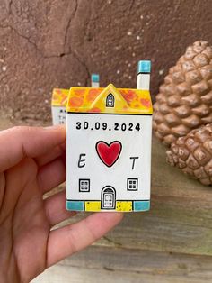 a hand holding up a small toy house with a heart on it's front