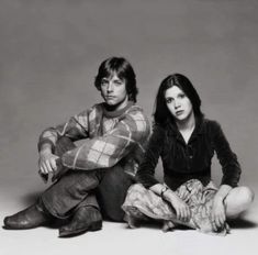 two people sitting next to each other on the floor in front of a gray background