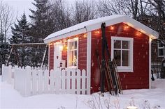 a small red house with lights on it's roof and snow covered yard in the foreground