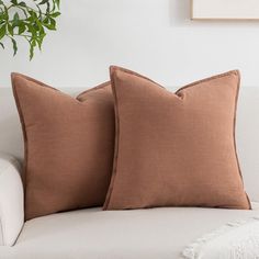 two brown pillows sitting on top of a white couch next to a potted plant