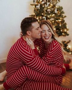 a man and woman in matching pajamas sitting on the floor next to a christmas tree