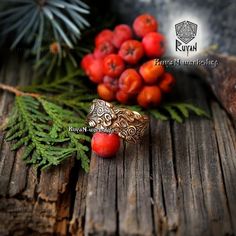 a close up of a ring on a wooden surface with berries and pine needles in the background