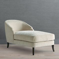 an upholstered chaise lounge chair in front of a gray wall and wooden floor