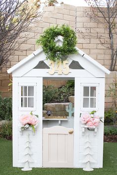 a small white house with flowers on the front door and windows in the back yard