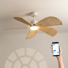 a person holding a cell phone up to a ceiling fan