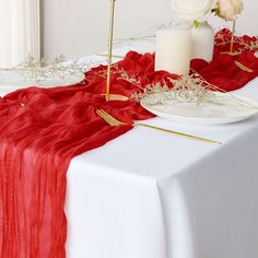 the table is set with red and white linens, gold place settings and flowers