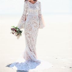 a woman is standing on the beach wearing a wedding dress and holding a bouquet in her hand