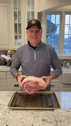 a man holding a raw piece of meat on top of a metal rack in a kitchen