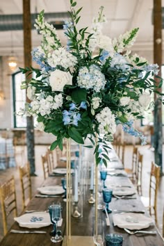 a tall vase filled with white and blue flowers sitting on top of a wooden table