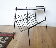 a black metal magazine rack sitting on top of a wooden floor next to a rug