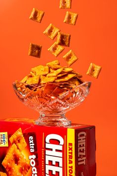 a box of cheeto crackers falling into the air over a bowl full of cheetos