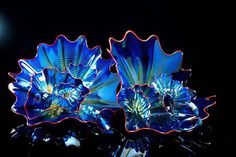 two blue glass vases sitting on top of a black table next to each other