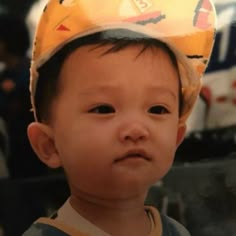 a small child wearing a yellow hat with cartoon characters on it's head and looking at the camera