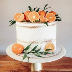 a white cake topped with orange slices and greenery on top of a wooden table