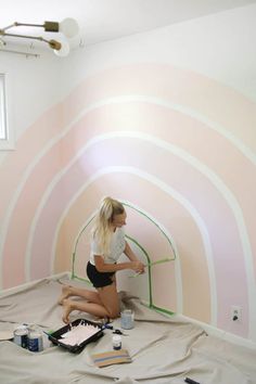 a woman painting a wall with pink and white stripes on the walls in a room