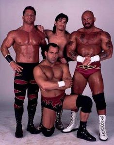 three men standing next to each other with one holding a wrestler's arm around the other