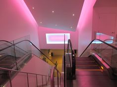 an escalator in a building with pink lighting on the ceiling and stairs leading up to it