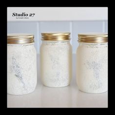 three white jars with gold lids sitting on a counter next to each other, one filled with salt and the other empty