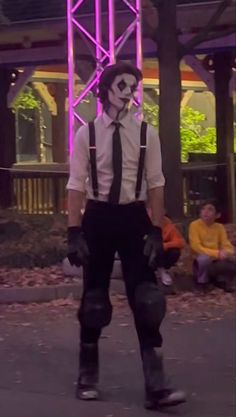 a man dressed up as the joker in front of a building with people sitting on benches behind him