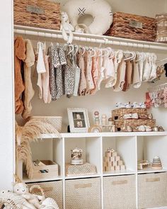 a closet filled with lots of baby clothes and baskets on top of white shelving