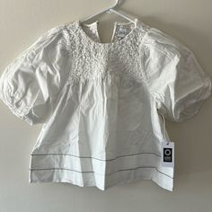 Our Armande Top Is The Fresh Pick Of The Season. The Bight White Top Has Puff Shoulders, A Smocked Neck Yoke, And Tiered Hem. Pair Armande With Your Favorite Denim For A Simple, Yet Put Together, Look. White Twill Self: 100% Cotton Unlined Shank Button At Back Of Neck Stretchy, Elastic Smocking Dry Clean Only Imported, India Model Is 5'9" And Wears A Size X-Small White Tops With Smocked Back For Daywear, White Smocked Bodice Blouse For Spring, White Blouse With Smocked Bodice For Daywear, White Tops With Smocked Back And Short Sleeves, White Puff Sleeve Blouse With Smocked Back, White Short Sleeve Tops With Smocked Back, Elegant White Puff Sleeve Top For Spring, White Cotton Puff Sleeve Top With Smocked Bodice, White Casual Puff Sleeve Top With Smocked Back