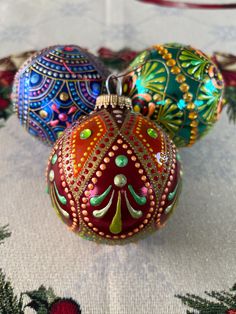 three christmas ornaments are sitting on a tablecloth with red, green and blue decorations