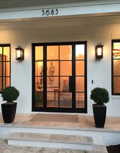 two large black planters are on the front steps of a white house with glass doors