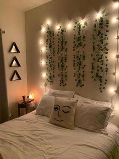 a white bed topped with lots of pillows next to a wall covered in plants and lights