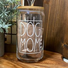 a dog mom jar sitting on top of a wooden table next to a potted plant