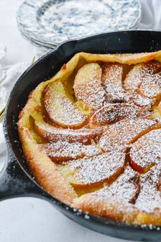 an apple pie is in a cast iron skillet on a table with plates and utensils