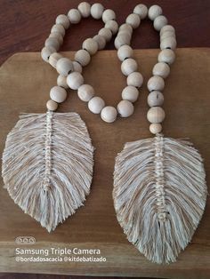 two necklaces made out of wood beads and white shells on a wooden board with the words samsung triple camera