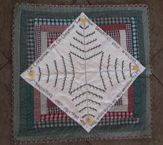 a quilted table topper on the floor with an embroidered leaf and flower design