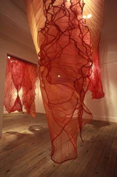 an art installation with red fabric hanging from the ceiling and wood flooring in front of it