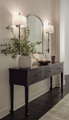 a table with a mirror, vase and candle on it in front of a wall