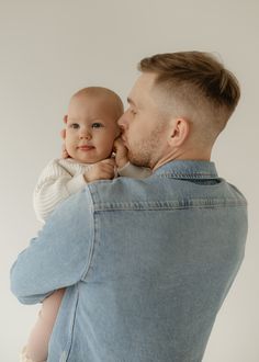 a man holding a baby in his arms and kissing it's face with the other hand