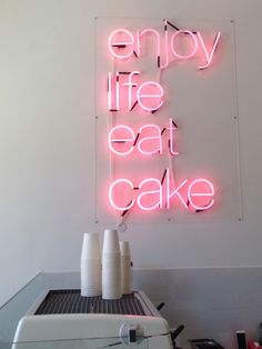 a neon sign that says enjoy life eat cake on the wall above a toaster