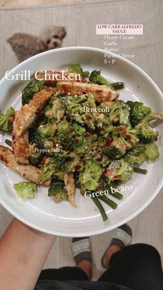 a white plate topped with broccoli covered in meat and sauces next to a person's feet