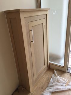 an unfinished bathroom cabinet with the door open and toilet paper on the floor next to it