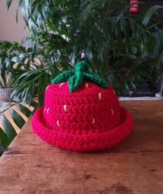 a crocheted strawberry hat sitting on top of a wooden table next to a potted plant