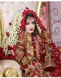 a woman dressed in red and gold sitting on a chair with flowers around her head