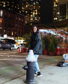 a woman standing next to a fire hydrant in the middle of a city at night