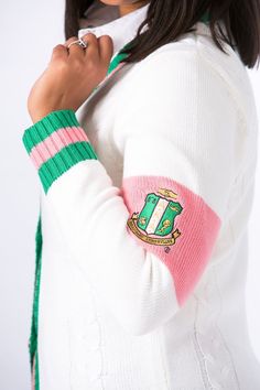 a woman wearing a white sweater with a green and pink stripe around her arm, posing for the camera