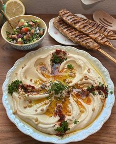 a table topped with plates and bowls filled with hummus next to grilled meat