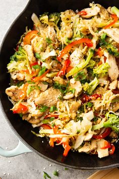 a skillet filled with chicken, broccoli and peppers