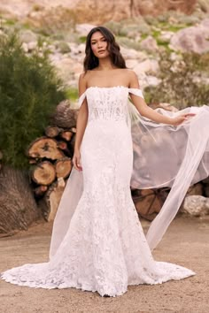 a woman in a white wedding dress holding a veil over her shoulder and posing for the camera