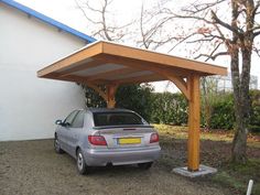 a car is parked under a wooden carport in front of a white wall and trees