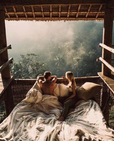 two people sitting on a bed in the middle of an open area with mountains and trees